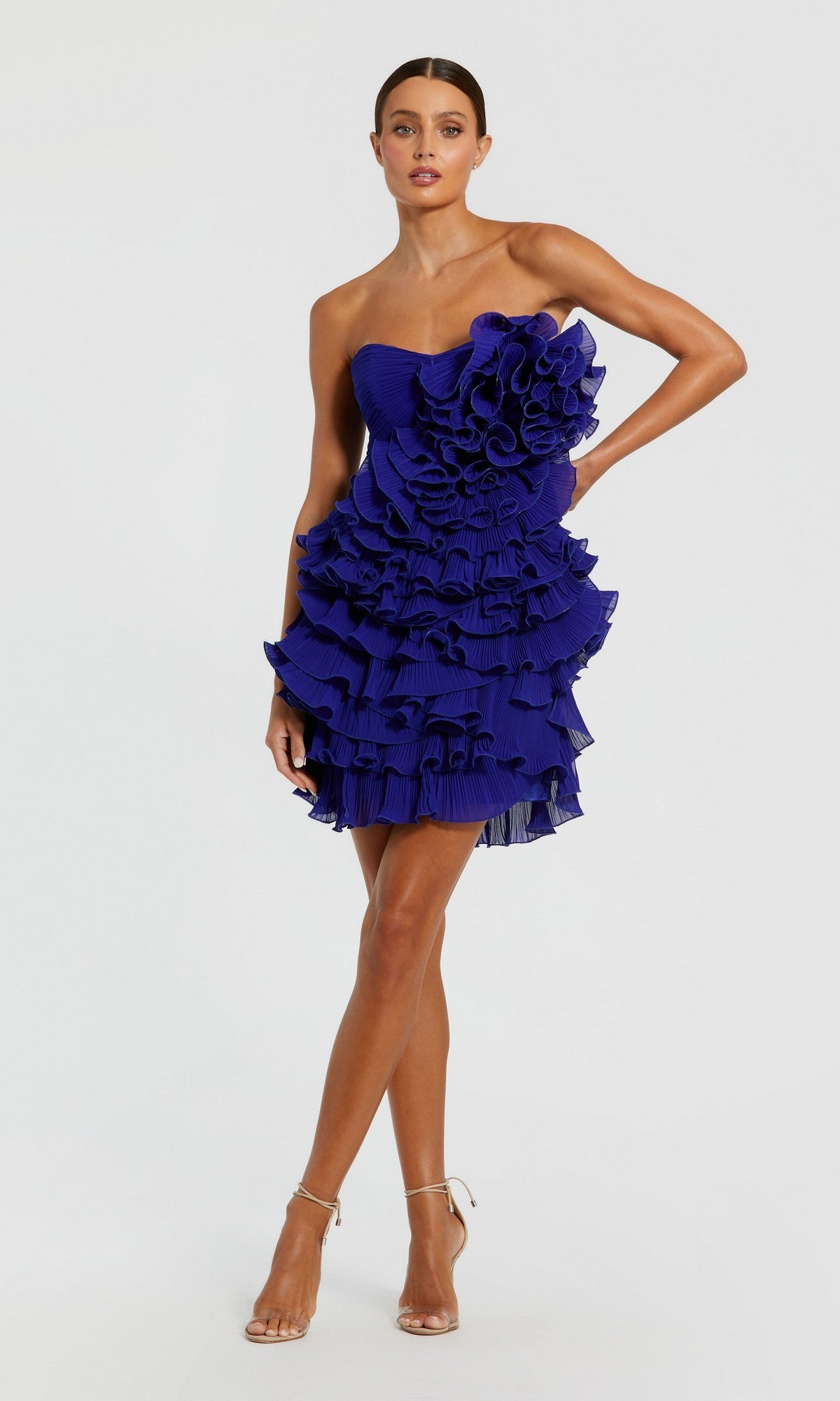 A woman poses in the Mac Duggal 11766 short party dress—a strapless, cobalt tiered ruffle mini—paired with nude high-heeled sandals against a plain background.